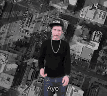 a man wearing a black hat and a black sweater is standing in front of a city .