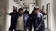 a man with a k on his jacket stands in a hallway with other men