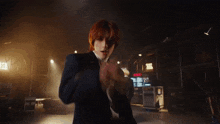 a man with red hair is standing in a dark room with lights behind him