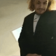 a man with long hair and a mustache is wearing a suit and tie .