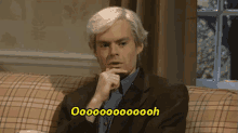 a man in a suit sits on a couch with a yellow sign that says ooooooh