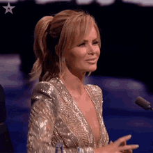 a woman in a gold dress is sitting in front of a microphone on a stage .