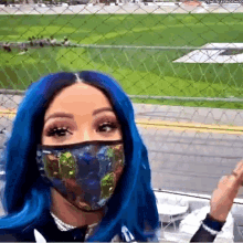 a woman with blue hair and a face mask is standing in front of a chain link fence .