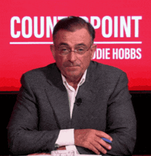 a man in a suit sits in front of a red sign that says count point