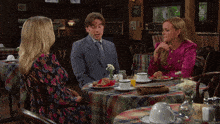 a man in a suit sits at a table with two other women