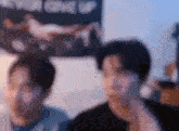 a blurry picture of two men sitting next to each other in front of a wall .