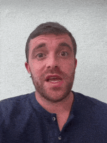 a man with a beard wearing a blue shirt making a funny face
