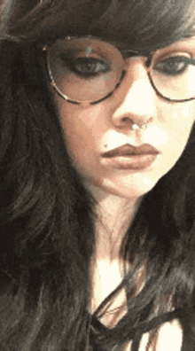 a woman wearing glasses and a nose ring is looking at the camera