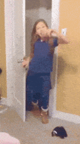 a girl in a blue shirt is standing in a doorway making a funny face