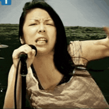 a woman singing into a microphone with a blue t on the bottom right