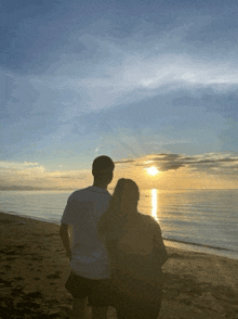 a man and a woman standing on a beach watching the sun set