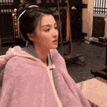 a woman in a purple blanket is sitting on a bed .