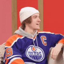 a young man wearing an oilers jersey and a white beanie