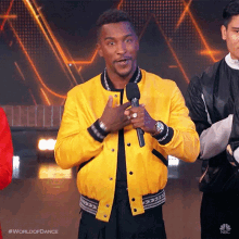 a man in a yellow jacket is holding a microphone and has the word world of dance on his shirt