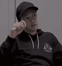 a man wearing a black hat and a black hoodie is holding a white marker .