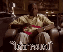 a man is sitting in a chair eating popcorn from a bowl .