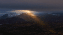 the sun shines through a cloudy sky over a mountain range