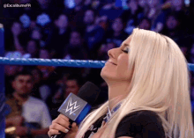 a woman in a wrestling ring is holding a microphone with a w logo on it .