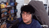 a man wearing glasses and headphones is sitting in front of a microphone in a room .