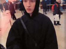 a man wearing a black hooded jacket stands in a crowd