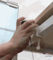 a person 's hand is reaching for something under a cabinet and the word petstone is on the bottom