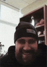 a man with a beard wearing a black beanie is smiling
