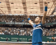 a man in a blue shirt is raising his arms in the air in front of a sign that says gerry weber