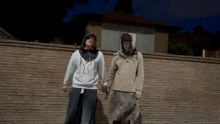 a man and a woman are standing next to each other holding hands in front of a brick wall .