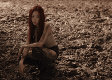 a woman with red hair is kneeling in a muddy field
