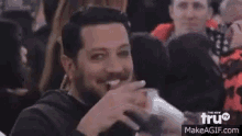 a man with a beard and mustache is sitting in a crowd of people and smiling .