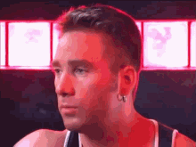 a man with earrings on his ear is looking at the camera in a dark room .