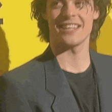 a close up of a man 's face with a yellow background . he is wearing a suit and smiling .