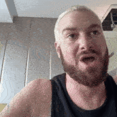 a man with a beard wearing a black tank top is making a funny face