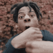 a man with dreadlocks is making a surprised face while holding his hands to his mouth .