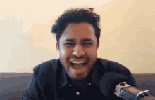a man with a mustache is laughing while sitting on a couch in front of a microphone .