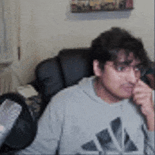 a man wearing an adidas sweatshirt is sitting in a chair