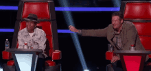 a man in a hat is sitting next to a man in a suit in a chair on a stage .