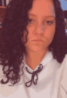 a woman with curly hair is wearing a white hoodie with a black knot around her neck