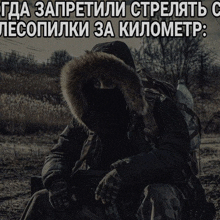 a man in a black jacket with a fur hood is sitting in a field with a foreign language caption