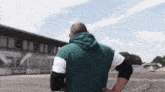 a man in a green hoodie stands in front of a building that says facom on it