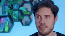 a man with a beard looks at the camera in front of a wall of displays