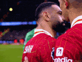 a man in a red shirt with the name shah on the back is hugging another man