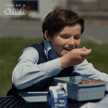 a boy is sitting at a table with a carton of 2 milk