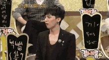 a man in a black jacket sits in front of a sign that says ' g dragon ' on it
