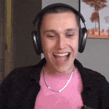 a man wearing headphones and a pink shirt is laughing and sticking his tongue out .