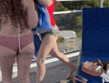 a woman in a bikini stands next to another woman in a red shirt