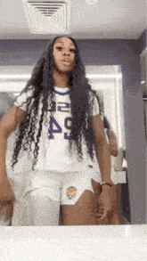 a woman with long hair is standing in front of a mirror wearing shorts and a white shirt .