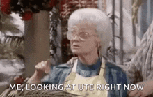 an elderly woman wearing glasses and an apron is sitting on a couch and looking at ute right now .