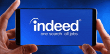 a person holding a cell phone with the indeed logo on the screen