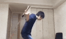 a man in a blue shirt is holding a stick in his hand in a room .